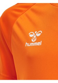 Camiseta deportiva naranja hecha de tejido suave, con un logo blanco de "hummel" en el lado izquierdo del pecho. Diseño de manga corta.