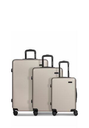 Trois valises rigides beiges avec des poignées noires et quatre roulettes, disposées de la plus grande à la plus petite, toutes équipées de poignées télescopiques extensibles.