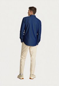 Dark blue button-up shirt with long sleeves, white buttons, and a smooth texture, paired with light-colored pants and beige sneakers.