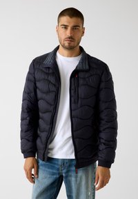 Marineblaue Steppjacke mit gesteppter Optik, die einen gerippten Kragen und ein kontrastierendes graues Innenfutter aufweist, vollendet mit einem Reißverschluss und Taschen.