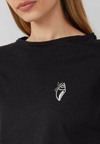 Zwarte katoenen t-shirt met een ronde hals, voorzien van een witte schelpgrafiek en het woord "cubra" in een gestileerd lettertype.
