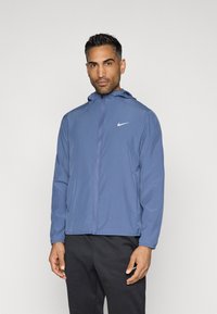 Μπλε φούτερ της Nike με κουκούλα, μπροστινό φερμουάρ, μακριά μανίκια και λευκό λογότυπο στο αριστερό στήθος. Λείο υλικό και ελαφρύ σχέδιο.