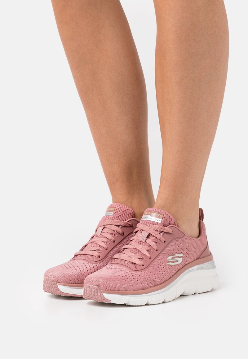 Rosa sportskor med överdel i mesh, texturerad yta och vit gummisula. Funktioner inkluderar en vadderad krage och snördesign.