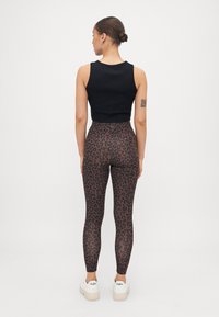 Crna bezrukavna crop majica u kombinaciji s smeškastim tajicama u smešak leopard uzorku, koje imaju visoki struk i glatku teksturu. Bijele platforme završavaju izgled.
