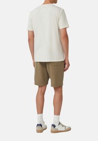 Jasno beżowa koszulka z krótkim rękawem, w zestawieniu z oliwkowymi, teksturowanymi szortami oraz białymi trampkami z granatowymi akcentami i beżową podeszwą.