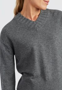 Grijze gebreide sweater met een v-hals, geribbelde kraag en lange mouwen. Zachte textuur en een ontspannen pasvorm, met een geribbelde zoom.