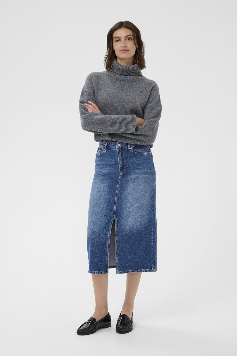 Harmaa slipover, keskikokoinen neule, yhdistettynä siniseen farkku-midi-hameeseen, jossa on edessä halkio. Mustat loafersit täydentävät asua.