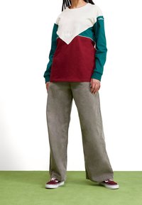 Långärmad sweatshirt med färgblockering i vit, grön och vinröd med texturdetaljer; matchad med ljusgrå vida byxor och vinröda sneakers.