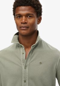 Hellgrünes Poloshirt aus strukturiertem Stoff, mit einer Drei-Knopf-Leiste und Logo-Stickerei auf der linken Brust.