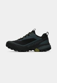 Zapatilla de trail running con un upper transpirable en negro y gris, suela resistente con surcos profundos y detalles en verde oliva.