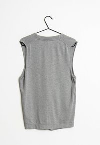 Grå ärmlös sweatshirt med rund hals och ribbade axeldetaljer, gjord av mjukt tyg, hängande på en svart metallhängare.