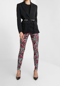 Svart kavaj med bälte i midjan, i kombination med färgglada leggings med blommönster i röd och blå, samt svarta pumps med spetsiga tår.