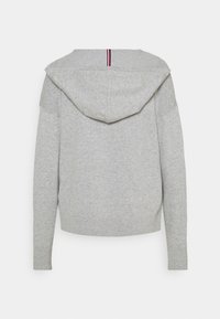 Sweat à capuche gris clair à manches longues avec un ourlet côtelé et une petite bande verticale rouge, blanche et noire au dos de la capuche.