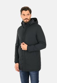 Parka nera con cappuccio, dotata di chiusura a zip e bottoni, caratterizzata da tasche laterali e una texture liscia e opaca. Adatta per il freddo.