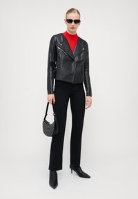 Veste en cuir noir de motard, turtleneck rouge à côtes, pantalon noir ajusté, sac à main en maille, et bottes noires à talons pointus.