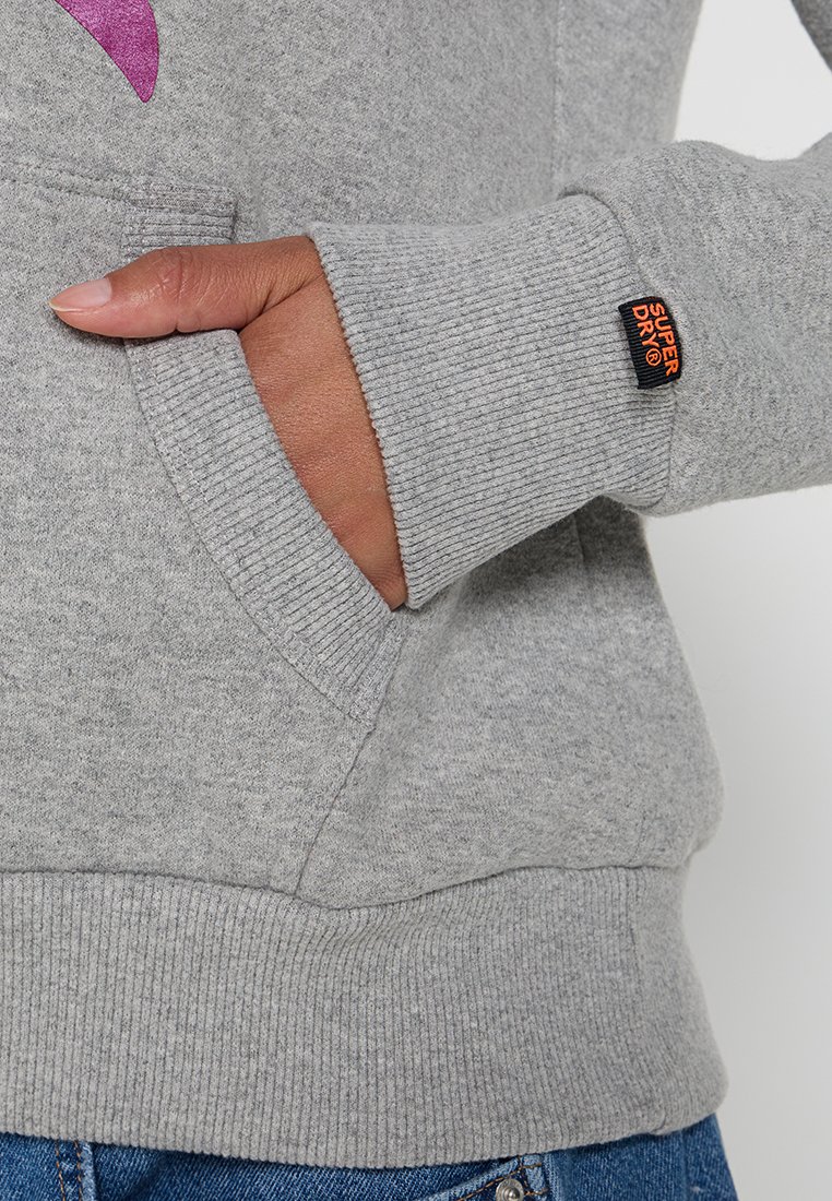 Felpa grigia con polsini e orlo a costine. Presenta una tasca a marsupio e un'etichetta nera con testo arancione, evidenziando una superficie liscia.