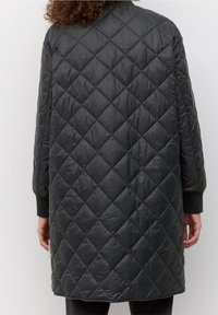 Abrigo acolchado negro aislante con un patrón de diamantes, que presenta un corte holgado, mangas largas y puños acanalados.