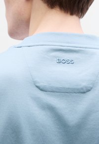 Ανοιχτομπλε βαμβακερό T-shirt με στρογγυλή λαιμόκοψη και λεπτή υφή. Διαθέτει κεντημένο λογότυπο "BOSS" στο πάνω μέρος της πλάτης.