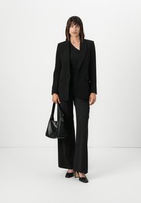 Blazer nero su una maglietta nera, abbinato a pantaloni larghi neri e décolleté a punta. Accessoriato con una borsa nera.
