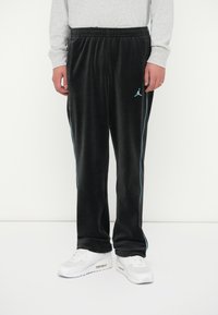 Juodi velūro kelnių su šviesiai mėlynomis šoninėmis juostelėmis ir išsiuvinėtu logo kairėje klubo pusėje. Elastingas juosmuo ir tiesaus kirpimo dizainas.