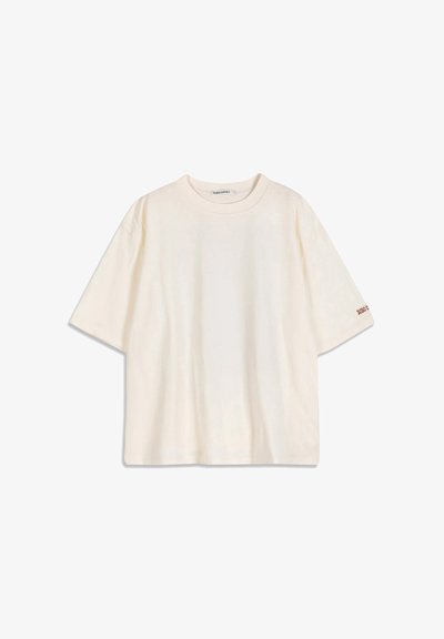 T-shirt en coton crème à manches courtes avec un col rond et un petit texte rouge sur le bord de la manche gauche.