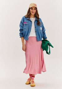 Džínsová bunda s nášivkou, biele tričko, ružová saténová sukňa, zelená kabelka a žlté tenisky s ponožkami so červenými pruhmi. Jednoduchý, neformálny outfit.