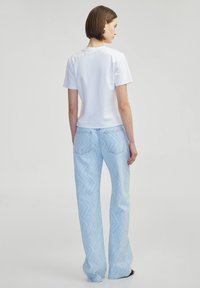 Top blanco de manga corta combinado con jeans acampanados de color azul claro que presentan un patrón en zigzag, un tejido texturizado y sutiles detalles de costura en la parte posterior.