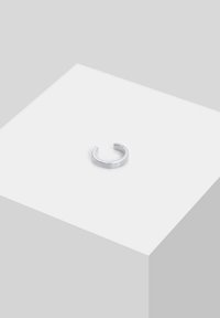 Anello in metallo argentato con superficie liscia e lucida, caratterizzato da un piccolo accento di pietra preziosa trasparente e un design aperto e regolabile.