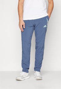 Pantalon de sport bleu en tissu léger, présentant une silhouette fuselée et des détails de marque subtils en bleu clair sur le côté.