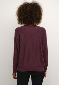 Burgundy tröja med lös passform, långa ärmar och ribbad nederkant. Mjuk textur, inga synliga mönster eller detaljer. Bakifrån vy visas.