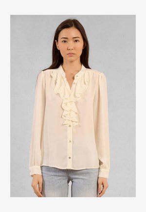 Blusa a maniche lunghe di colore avorio con un davanti arricciato, consistenza morbida e chiusura a bottoni. Tessuto leggero, spalle leggermente arricciate e orlo arrotondato.