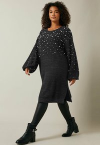Tummanharmaa neulottu mekko, jossa on helmikirjailuja, pitkät pallomaiset hihat, sivuhalkiot ja rento siluetti. Yhdistetty mustiin legginsseihin ja saappaisiin.