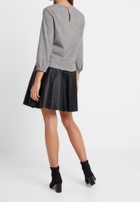 Haut à carreaux gris à manches longues avec un dos ajouré, associé à une jupe en similicuir noir. Bottines noires complètent la tenue.