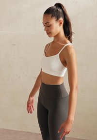 Baltas sporta krūšturis ar plāniem siksniņām un apaļu kakla izgriezumu, kopā ar augstvērtīgām, ribu faktūras, tumši pelēkām legingām. Gluda tekstūra, pieguļoša forma.