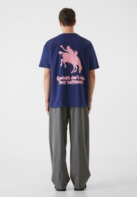 Mörkblå bomullströja med en rosa grafik av en cowboy på en häst och texten "Cowboys don’t nap. They caffeinate" på baksidan.