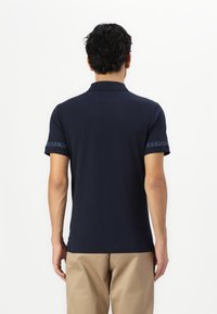 Polo de culoare bleu marin, cu guler și mâneci scurte, având un logo imprimat pe mâneca stângă. Material din bumbac neted, croială lejeră.