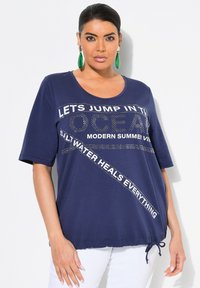 Navy blauwe t-shirt met korte mouwen en een tekstontwerp, verrijkt met strass-steentjes en een koordzoom voor een verstelbare pasvorm. Ontspannen silhouet.