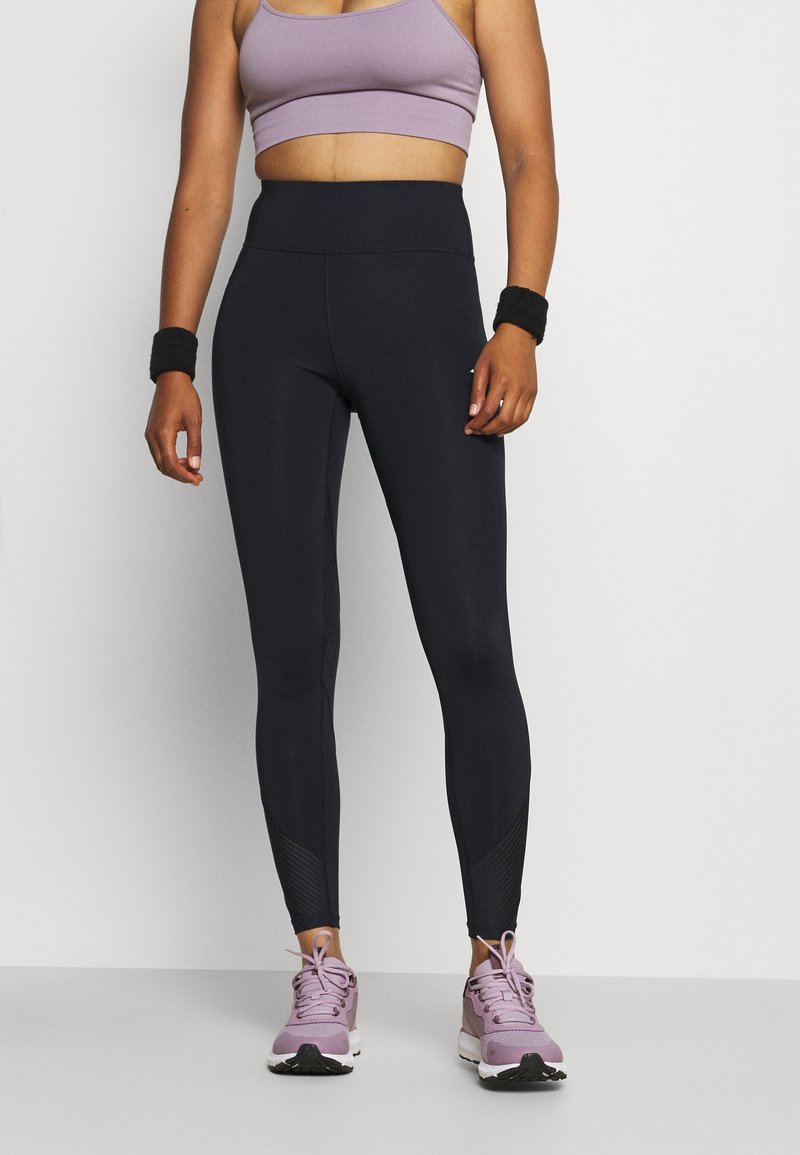 Czarne legginsy sportowe z wysokim pasem, z teksturowanymi akcentami przy kostkach. W zestawie z lawendowym stanikiem sportowym i fioletowymi trampkami.
