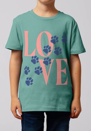 Enfant portant un T-shirt vert avec le mot « LOVE » en grandes lettres roses et des empreintes de pattes bleues dispersées sur le devant.
