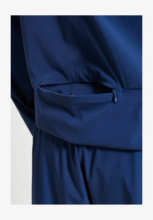 Nærbilde av et marineblått jakkelomme med glidelås delvis åpen på et plagg i matchende stoff.