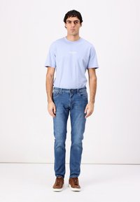 T-shirt en coton bleu clair avec col rond, assortie à un jean slim bleu. Des baskets en cuir marron complètent la tenue. Design simple, sans motifs.