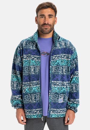 Fleece-Jacke mit einem geometrischen Muster in Blau, Türkis und Lila, Reißverschluss vorne und einem kleinen Logo-Patch auf der linken Seite.