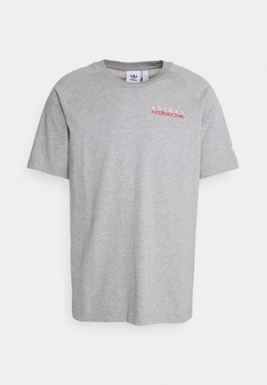 Camiseta de algodón gris con mangas cortas, cuello redondo y estampado "ADIDAS INTERNATIONAL" en rojo en el pecho. Diseño sencillo sin patrones adicionales.