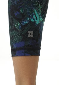 Leggings capri neri con un motivo astratto di foglie verdi e blu in texture, con un piccolo logo sul lato sinistro dell'orlo.