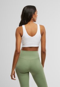 Hvit atletisk crop top med dyp ryggutskjæring, kombinert med høy midje, lysegrønne leggings laget av elastisk materiale. Glatt tekstur.