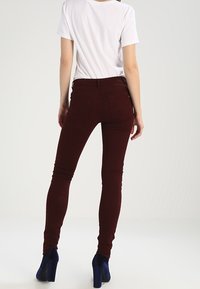 Burgundy skinny jeans med en slät yta, låg midja och två bakfickor, tillsammans med en enkel vit t-shirt och blå klackar.
