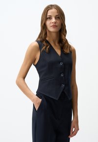 Marinefarbener ärmelloser Weste mit V-Ausschnitt, ausgestattet mit drei Knöpfen und seitlichen Taschen, aus glattem Stoff mit taillierter Passform.