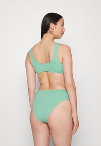 Conjunto de bikini verde menta com um top de costas em forma de concha e parte de baixo de cintura alta, feito de um tecido canelado com uma textura suave.