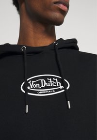 Svart hoodie med en vit broderad "Von Dutch Originals"-logotyp, med metallförsedda dragsnören och en mjuk tygstruktur.