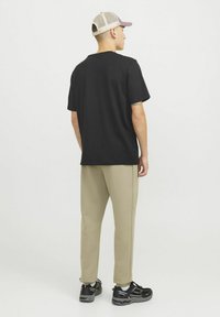 Black t-shirt with short sleeves, paired with beige tapered pants. The person wears a beige and pink cap and black athletic shoes.